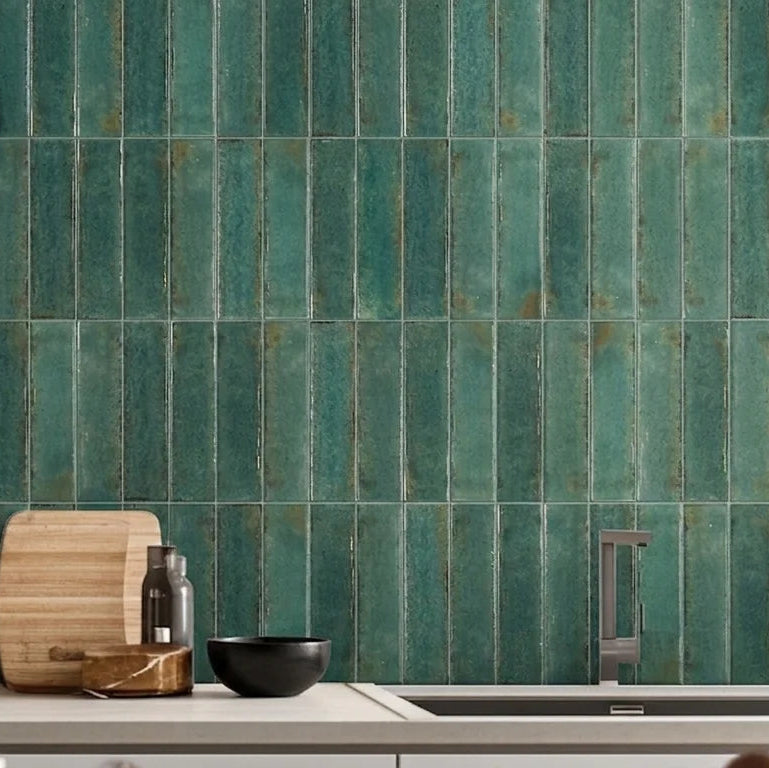 Vertical green ceramic subway tiles on a kitchen backsplash behind a light countertop with a pot, cutting board, and small bowls.