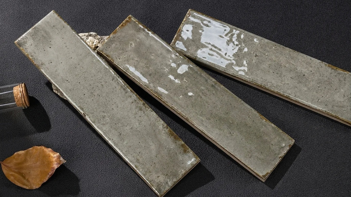 Three rectangular ceramic tiles with a textured, distressed gray finish and glossy white glaze accents, arranged diagonally on a dark textured surface.