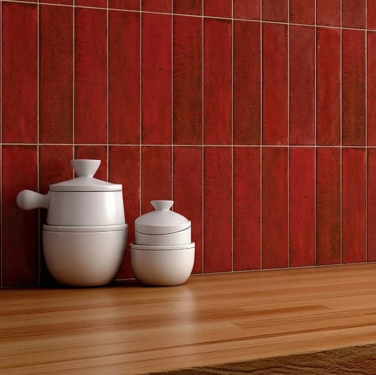Red glossy rectangular wall tiles on a kitchen backsplash above a wooden countertop, with white ceramic containers and a potted green plant.
