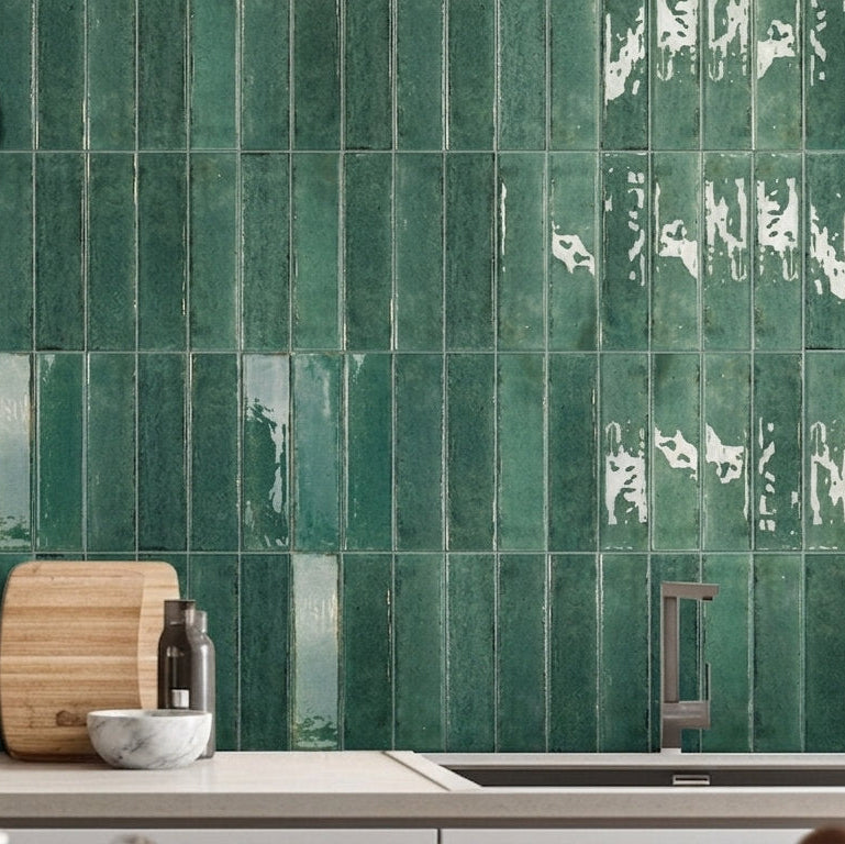 Green glossy rectangular subway tiles installed on a kitchen backsplash, with a countertop, pot, cutting board, and sink visible.