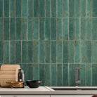 Vertical green ceramic subway tiles on a kitchen backsplash behind a light countertop with a pot, cutting board, and small bowls.