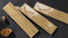 Three rectangular ceramic tiles with a textured beige and white marbled pattern, arranged diagonally on a dark textured surface next to a cork bottle and a dried leaf.